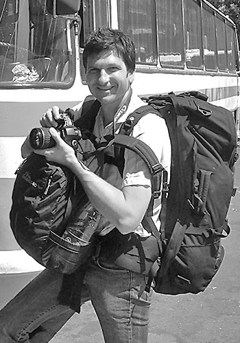 Photo of Artist Pisani with camera in hand while loaded up with backpack and camera bag while traveling in Eastern Europe.